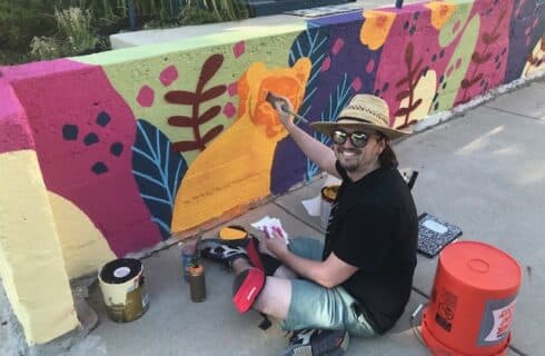 Photo of John Kowalczyk painting an outdoor mural on a wall at The Muse Gallery Guesthouse
