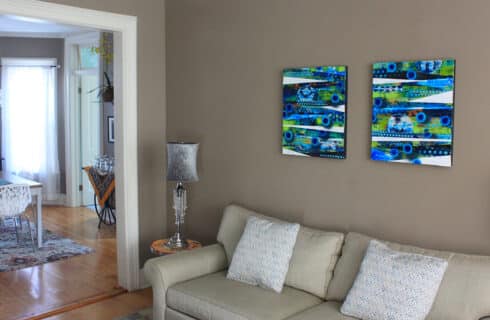 Bright abstract artwork on the tan walls of a lounge with upholstered couch. Wide white-trimmed doorway into a kitchenette dining area with a table and microwave.