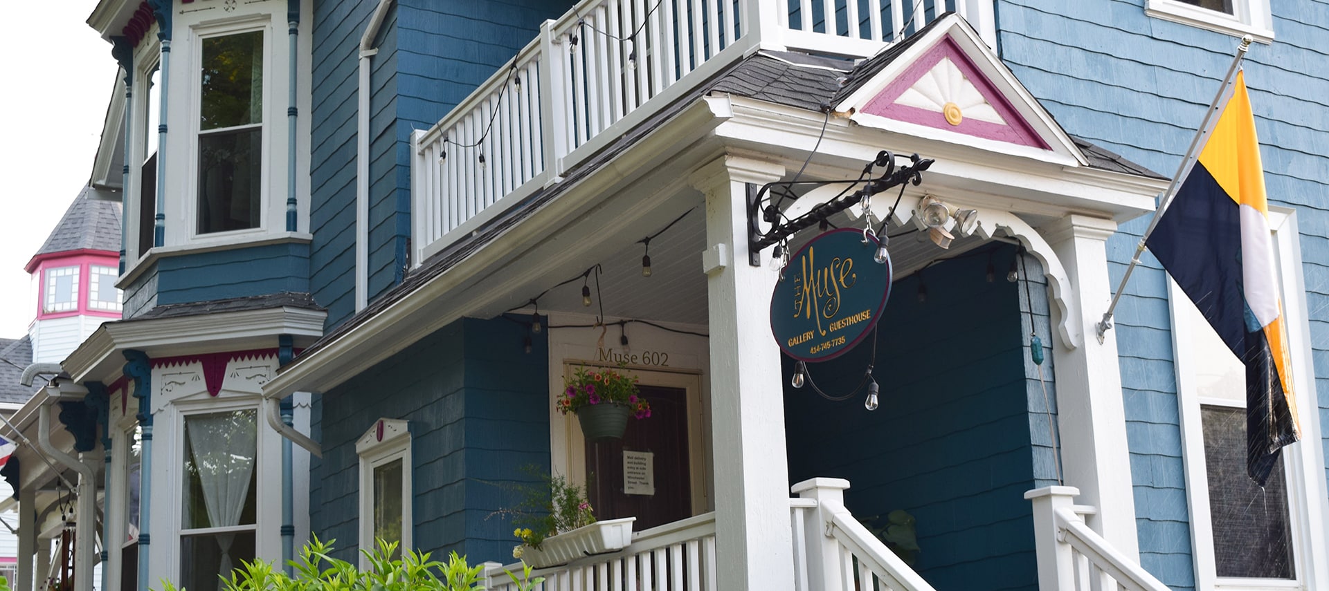 Corner view of the front and side facade of large blue Victorian house with white porch steps leading to the front door.