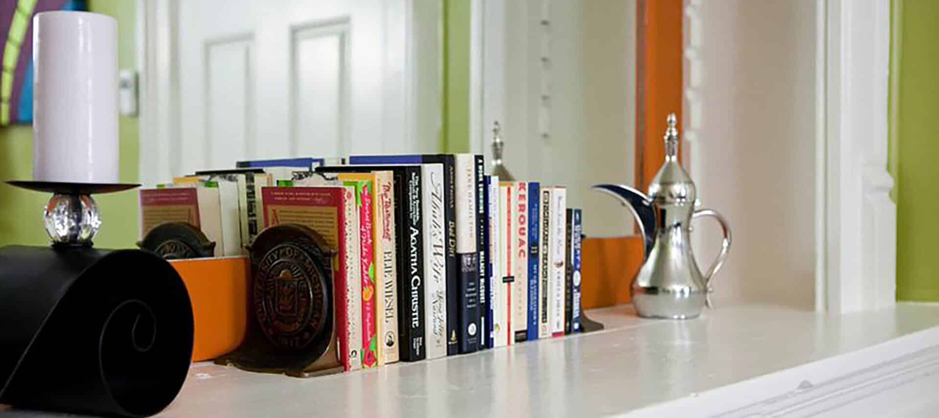 Row of books with brass bookends on a mantel in front of a mirror.