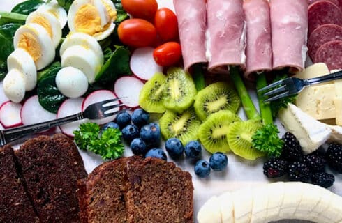 Breakfast tray with an array of breads, boiled eggs, meat, fruit, berries and vegetables.