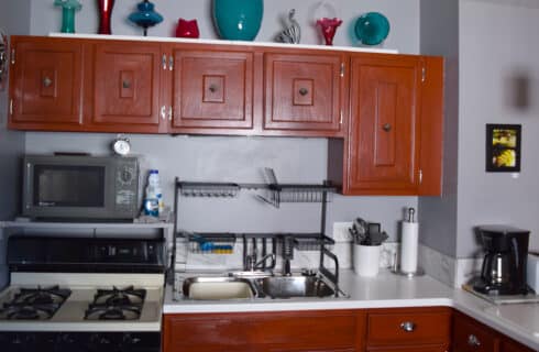 Kitchen with a stove and oven, sink, countertop, brown cabinets and decorative objects on top of the cabinets.