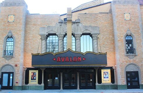 The facade of an orange-brick 1920's Moorish-revival-style movie palace with ornate windows and columns and a marquee with a neon sign that says Avalon