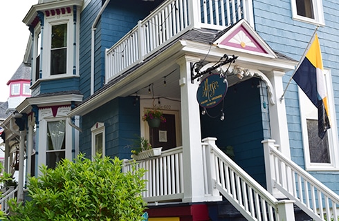 Large yellow house with shutters, porch with white railings leads to the front door and white picket fence.