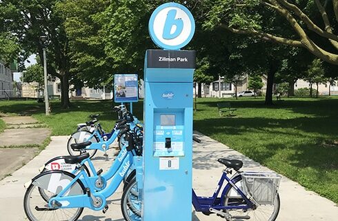 Blue Bublr bikes parked at a station on the sidewalk next to Zillman Park.
