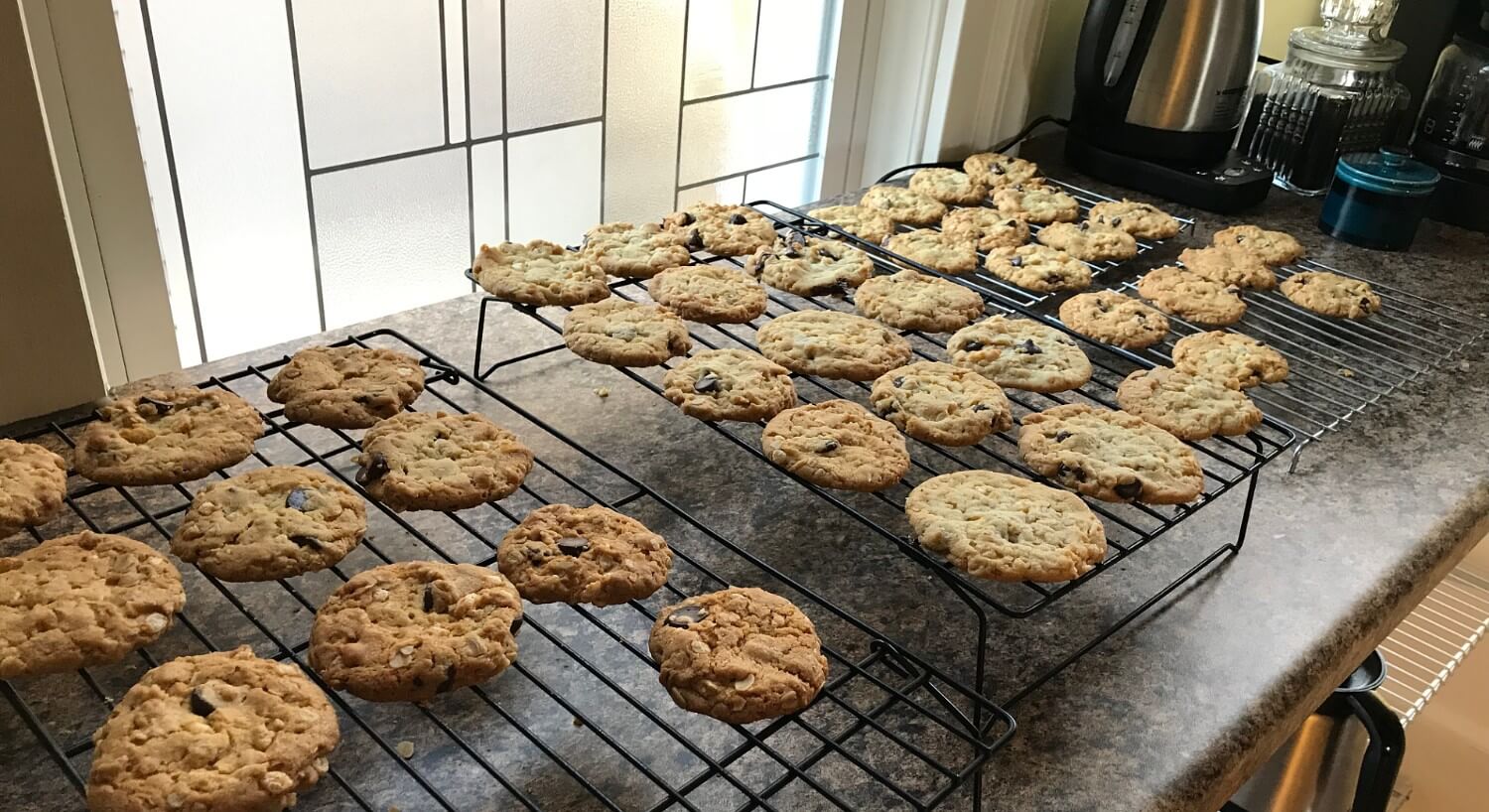 Chocolate chip cookies cooling on wire racks in front of a window.