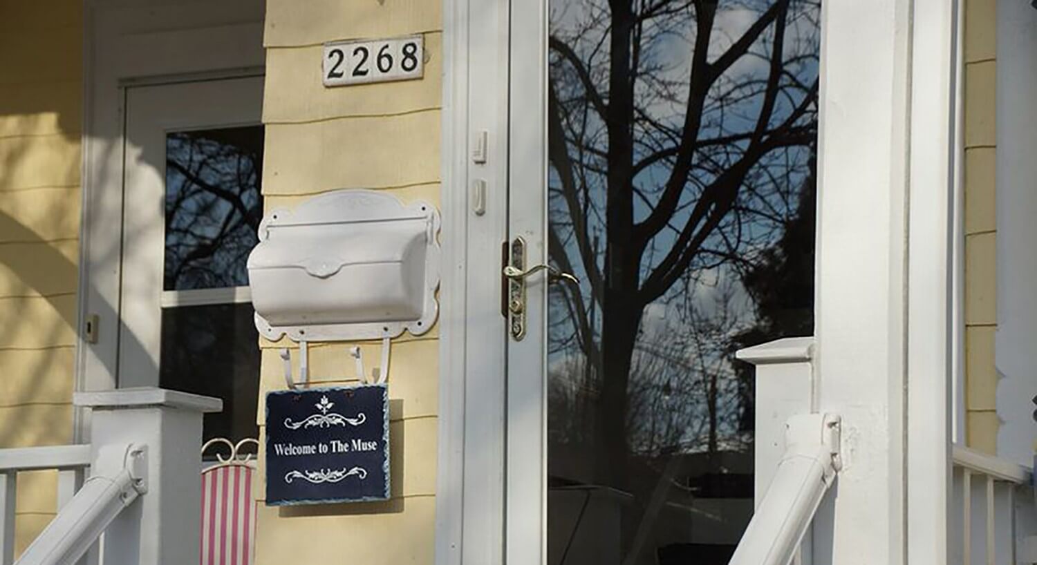 Front door of yellow house with white metal mailbox and sign that says, Welcome to The Muse.