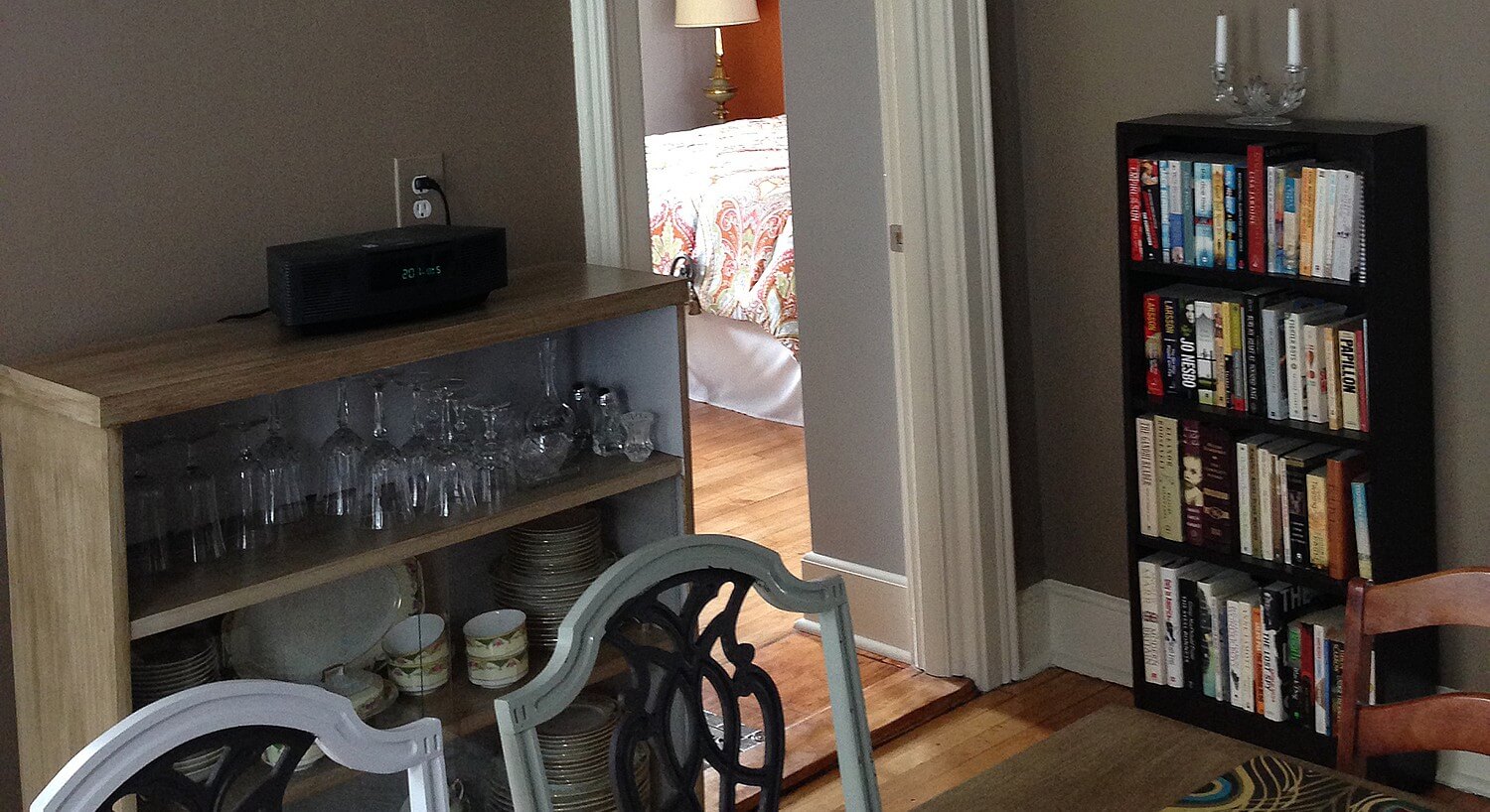 Bookcase with books and cabinet with china and glassware in a room with a table and chairs.