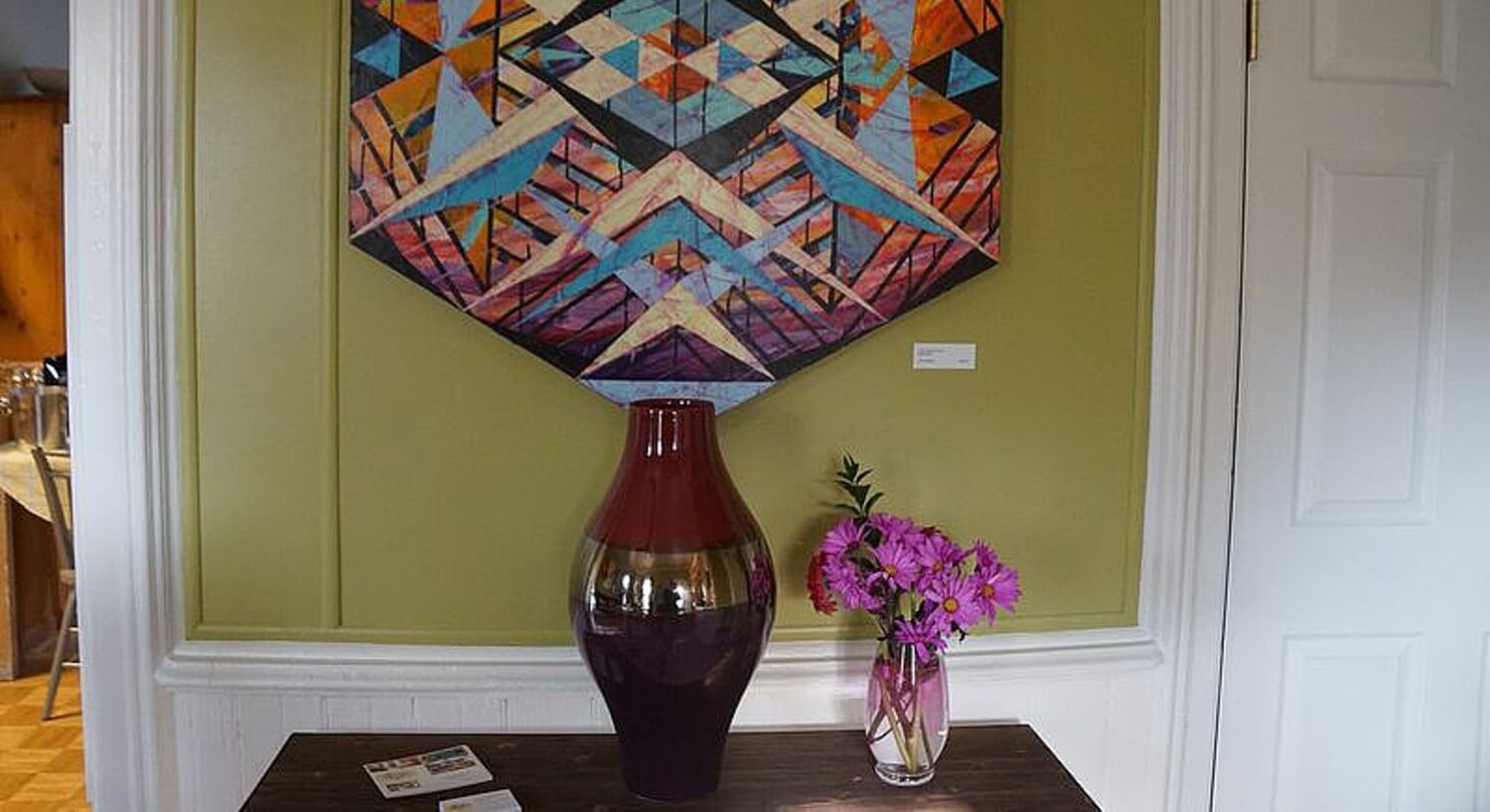 Decorative vase on wooden table under a modern art piece.