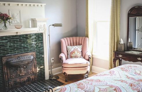 Tiled fireplace is the focal point of a bedroom with a bed, peach armchair and a vanity.
