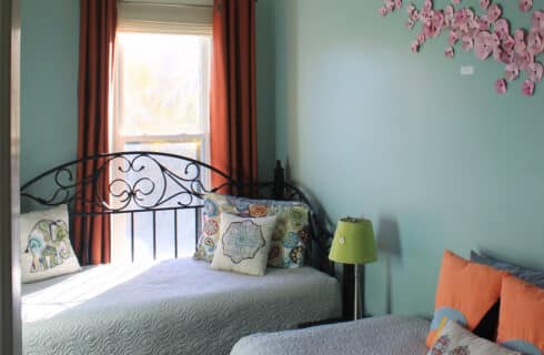 Daybed with patterned spread and pillows in a room with exuberant colorful art on the walls.