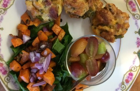 Roasted root vegetables with fruit salad and baked breakfast muffins on a china plate.