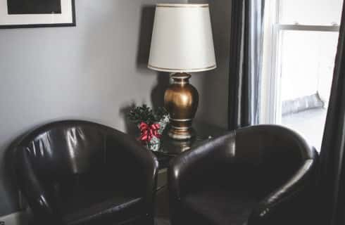 Two leather club chairs next to a window and table with a plant and a lamp.