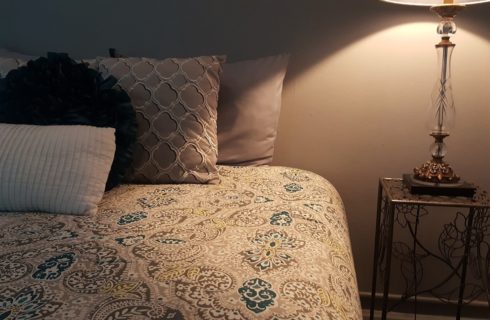 Paisley patterned spread on a bed next to a wire table with a lamp.