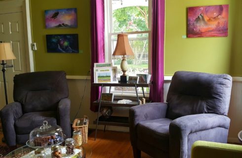 Two purple upholstered chairs in a lime green room sit beside a window with fuschia drapes.