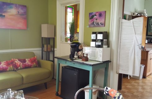 Green sofa in a room with art on the walls and swinging louvered doors to a kitchen.