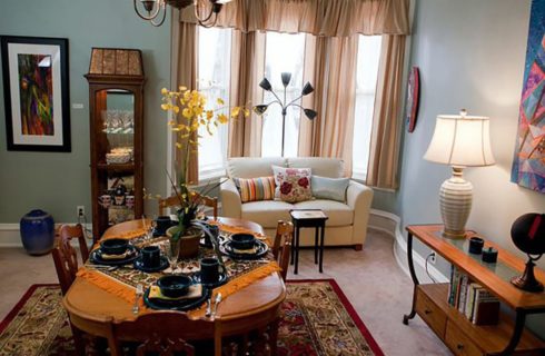 White sofa in front of a window with peach drapes in a room with a dining table and chairs.