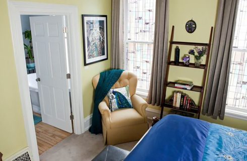 view from above of yellow bedroom with bed made up in blue and a wingback recliner.