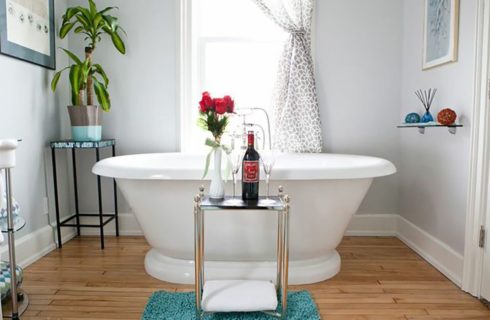 Bathroom in white with a soaking tub in front of a window with a patterned curtain.