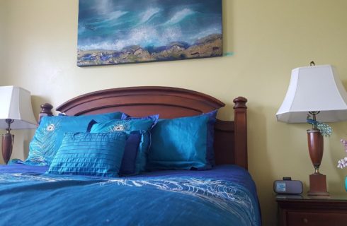 Cherry queen bed made up in peacock blue spread and shams with matching nightstands and lamps.