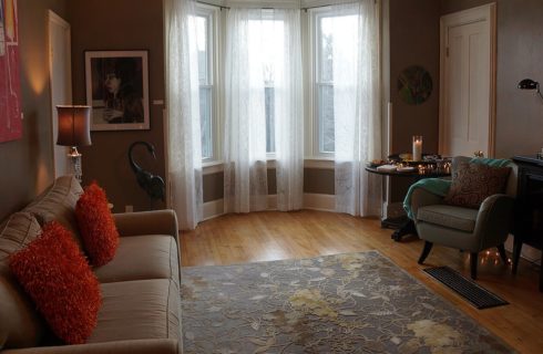 Room with bow window holds a beige sofa and chair with a large television.