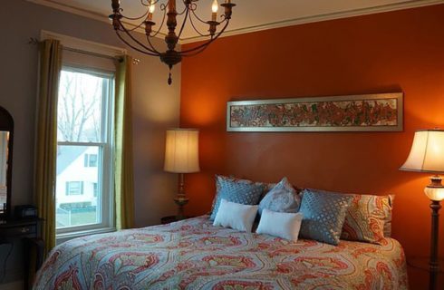 Guestroom with orange and blue walls with a queen bed and two nightstands with lamps.