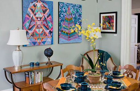 Original art pieces on the walls of a room with a table set for breakfast and console table.
