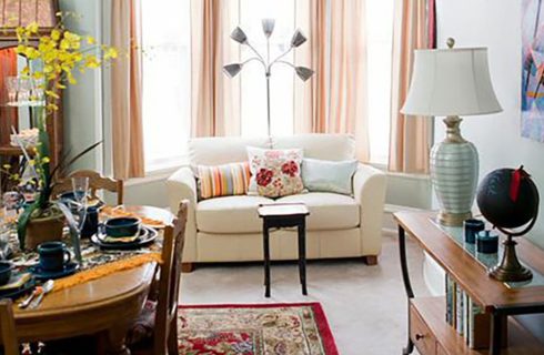 White sofa in front of a window with peach drapes in a room with a dining table and chairs.
