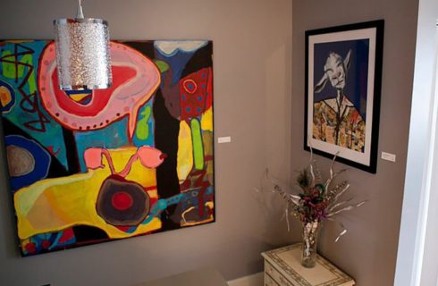 Original art pieces on the walls of a room with beige walls and a silver light fixture.