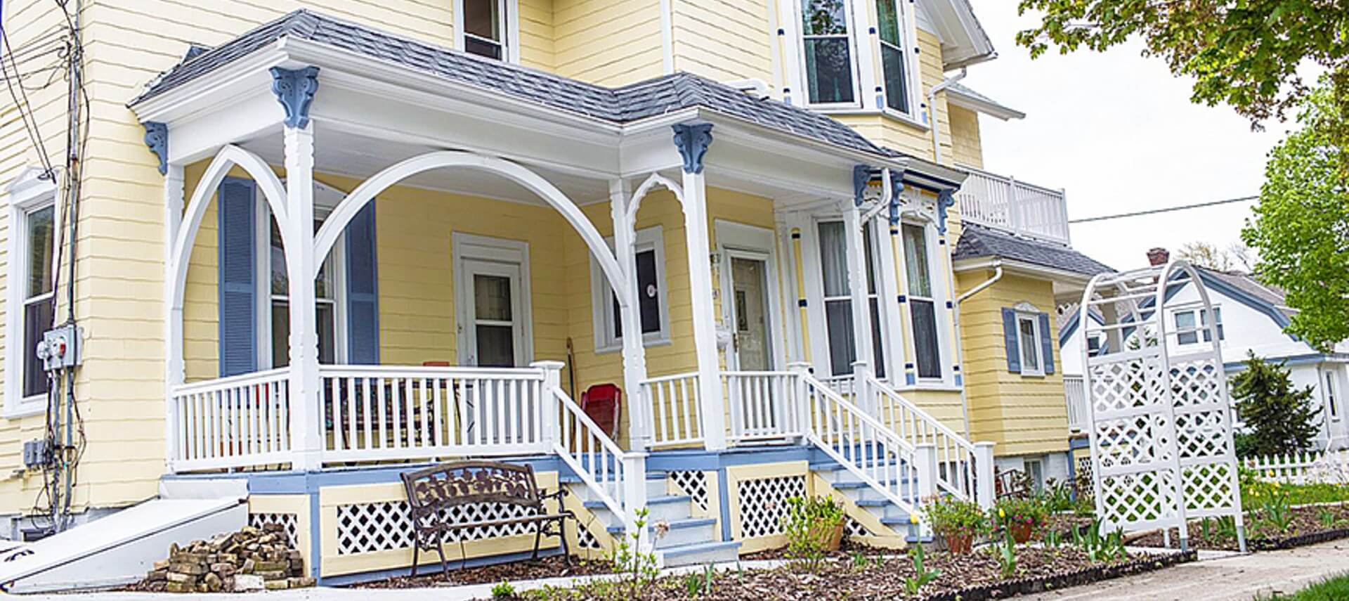 Large yellow house with shutters, porch with white railings leads to the front door.