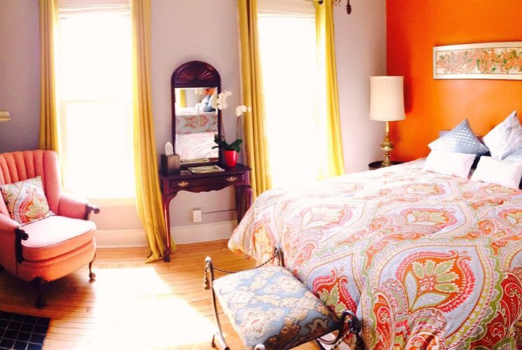 Unique guestroom with salmon colored walls, bed made up in a patterned comforter and a fireplace.