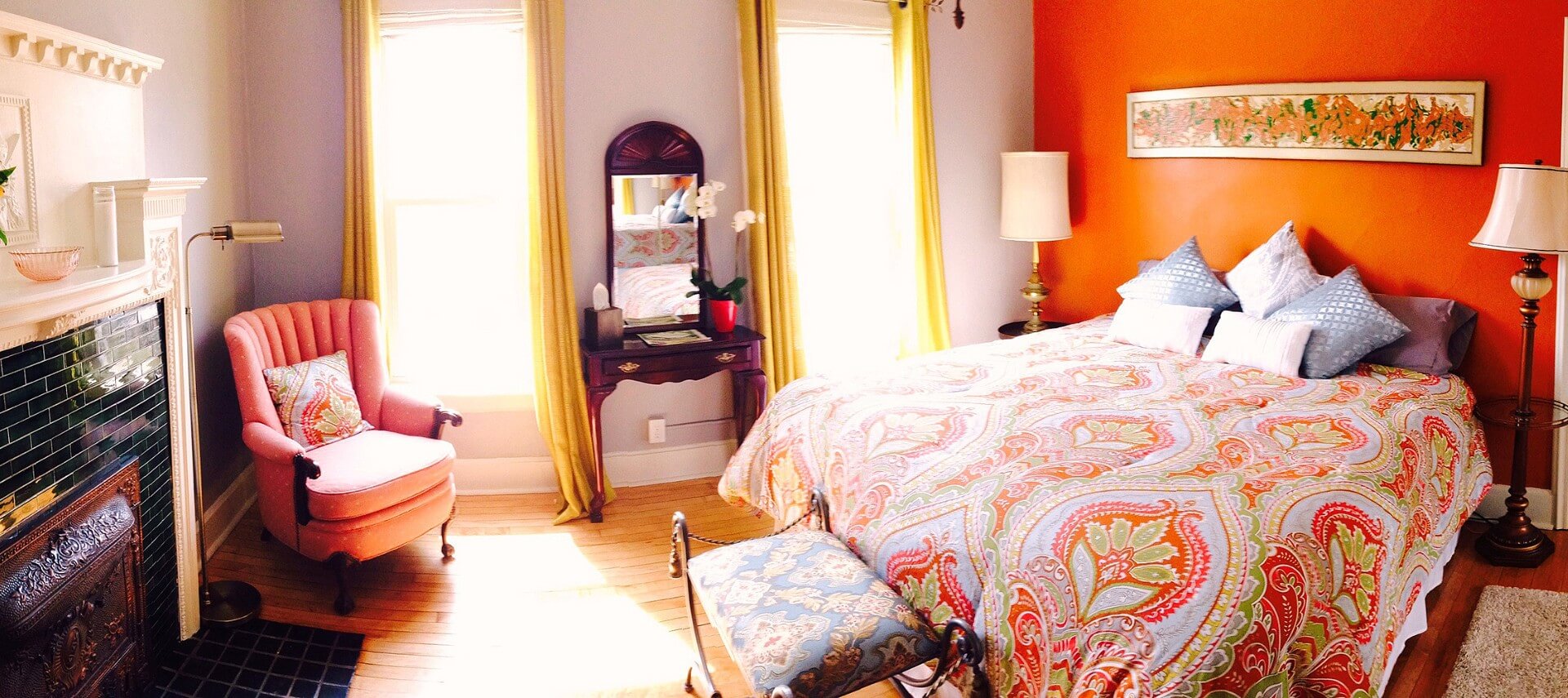Unique guestroom with salmon colored walls, bed made up in a patterned comforter and a fireplace.