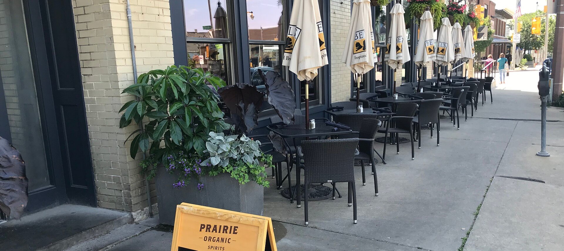 Black iron bistro tables and chairs set up outside a restaurant on a city street.