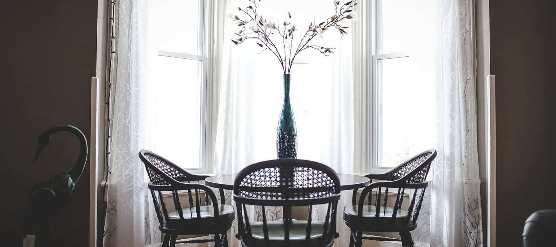Small table and chairs set in front of a bow window with gauze curtains.
