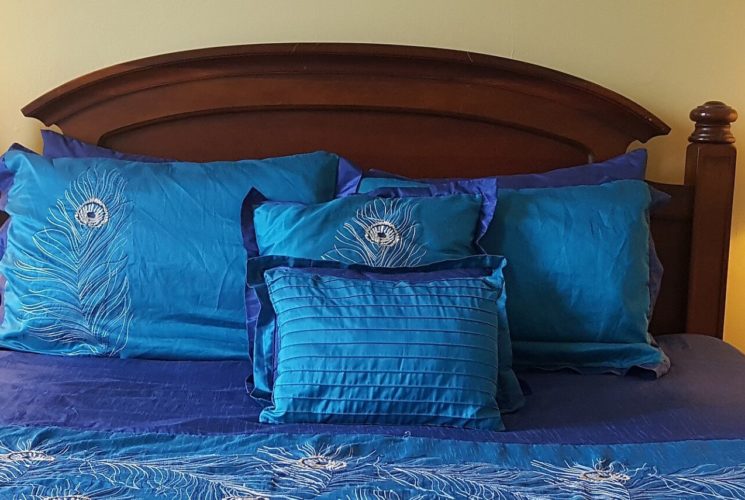 Cherry queen bed made up in peacock blue spread and shams with matching nightstands and lamps.