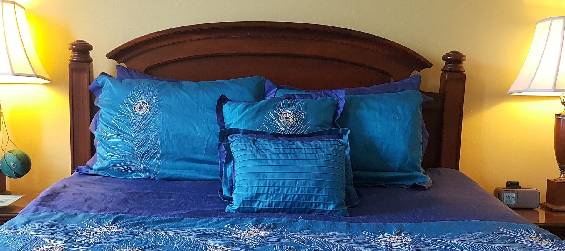 Cherry queen bed made up in peacock blue spread and shams with matching nightstands and lamps.