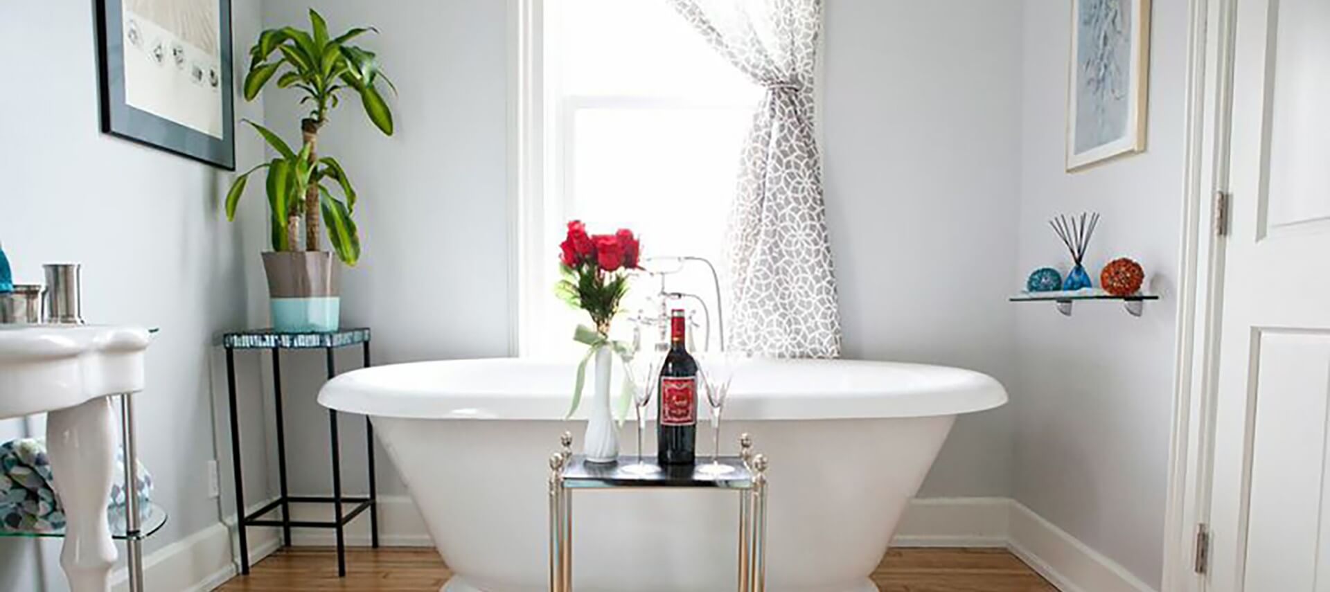 Bathroom in white with a soaking tub in front of a window with a patterned curtain.