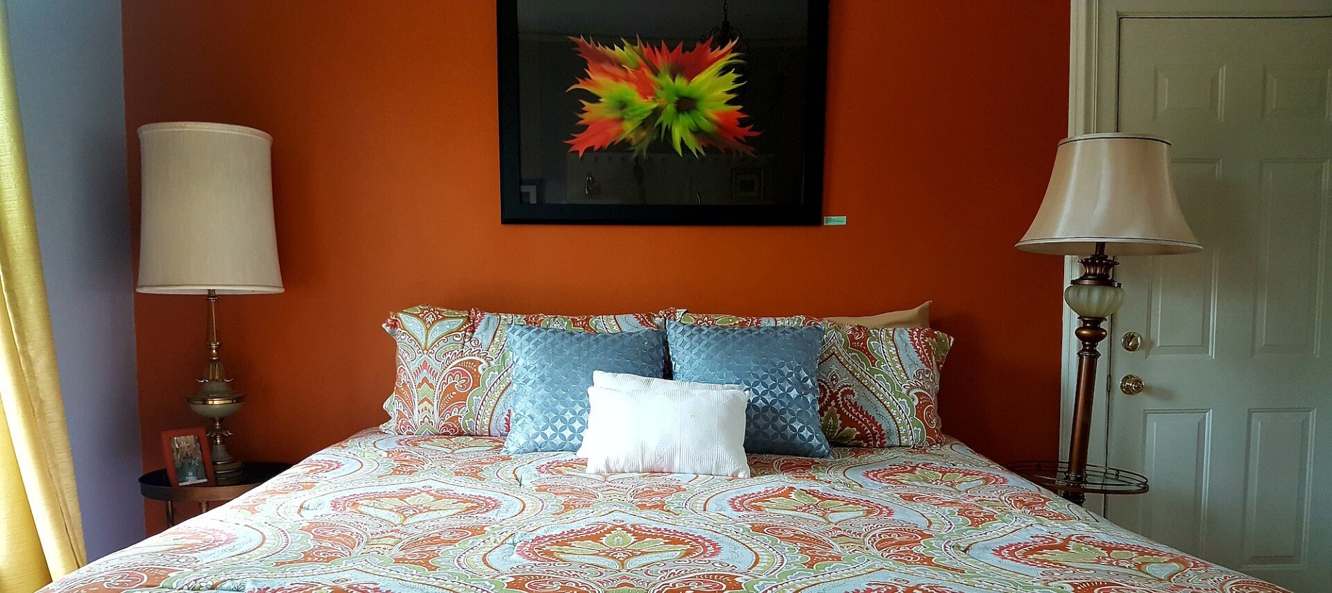 Guestroom with orange and blue walls with a queen bed and two nightstands with lamps.