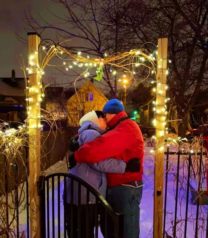 two people dressed in snow clothes kissing outside under the mistletoe