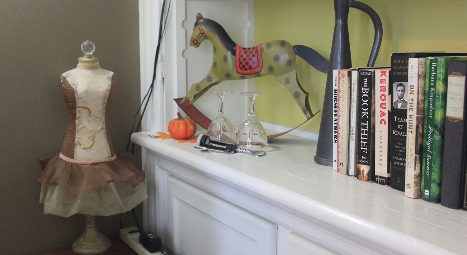 White built-in bookshelf with books, a horse sculpture, and a small sculpture of a dressmaker's dummy.