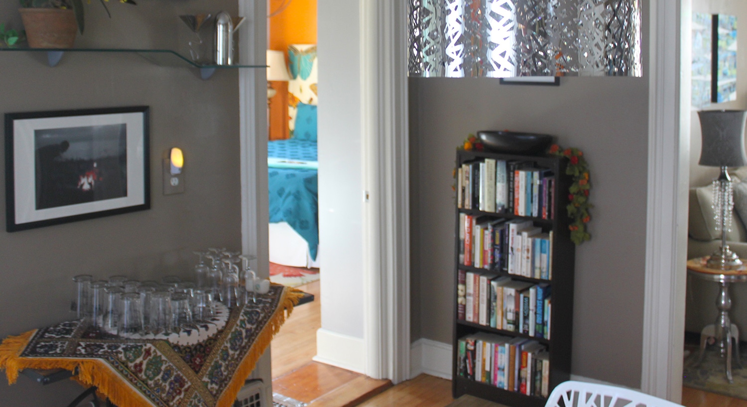 Bookshelf full of books in a room with grey walls, and white doorway into another room. A decorative silver metal lampshade.