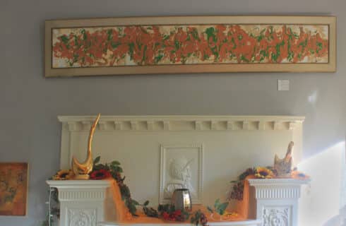 ornate white wood carved mantlepiece decorated with cloth and small sculptures. A wide abstract painting hangs on the grey wall above the mantle.